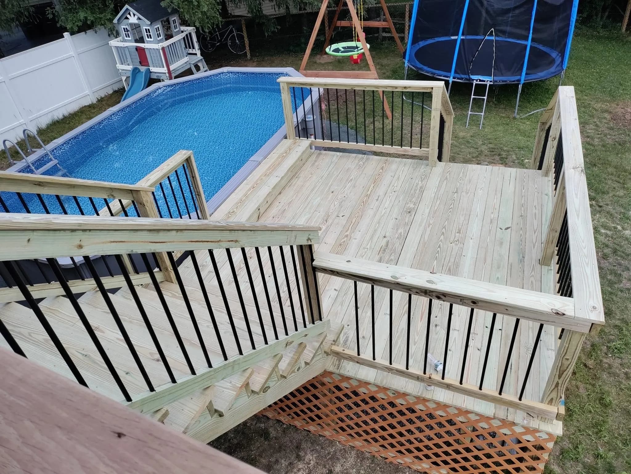 Multi-level wooden deck with above-ground pool, swing set, and trampoline