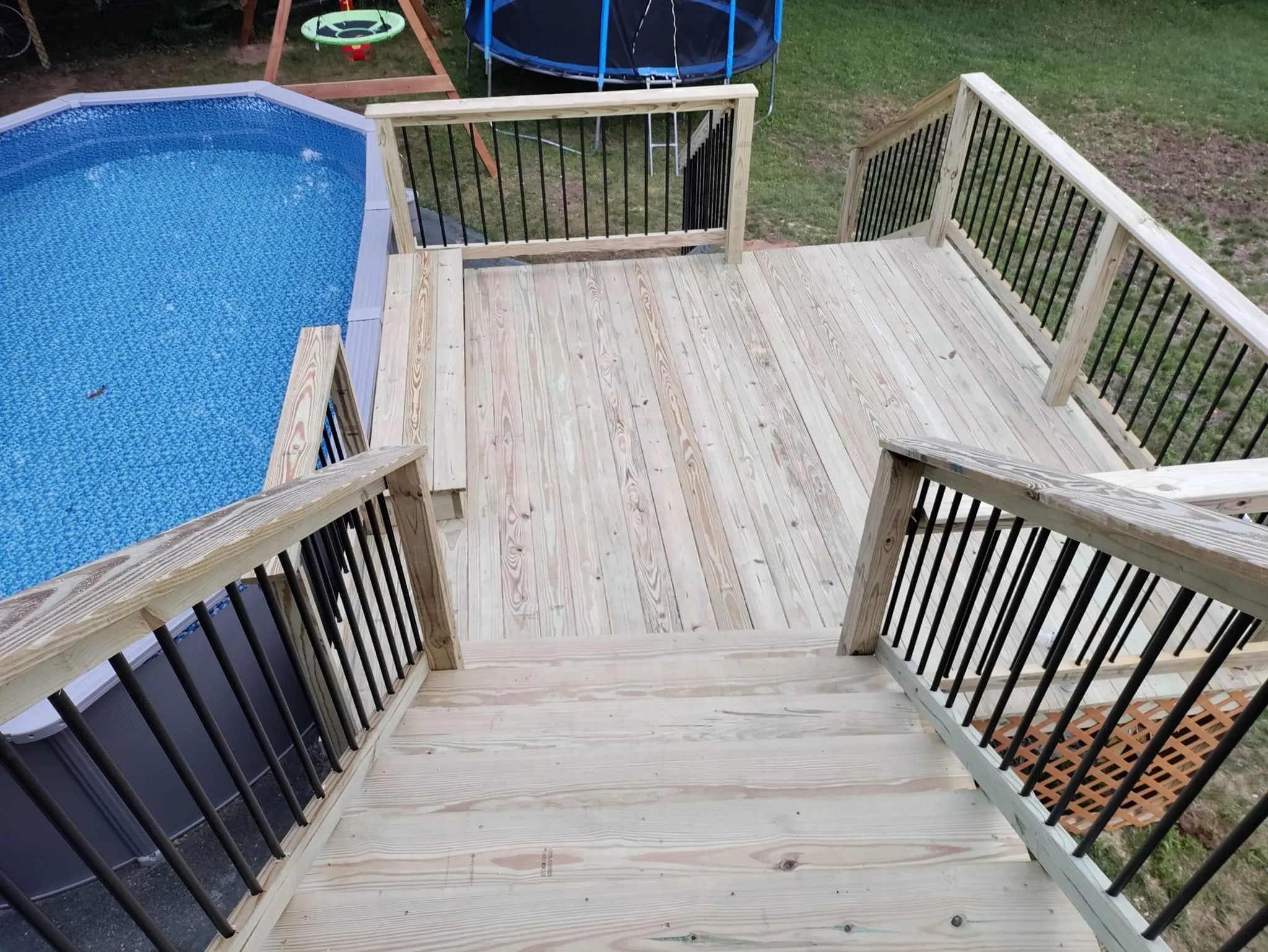 Pool deck with wooden boards, black railings, and play area