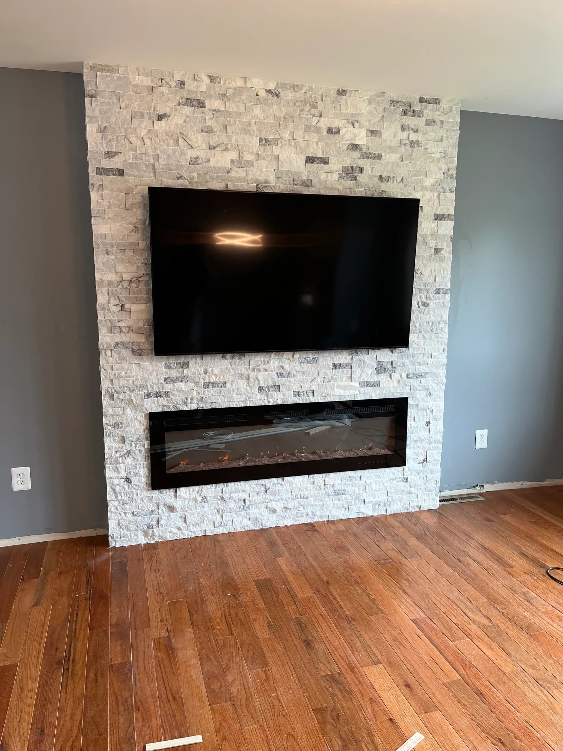 Stacked stone TV and electric fireplace wall with hardwood floor