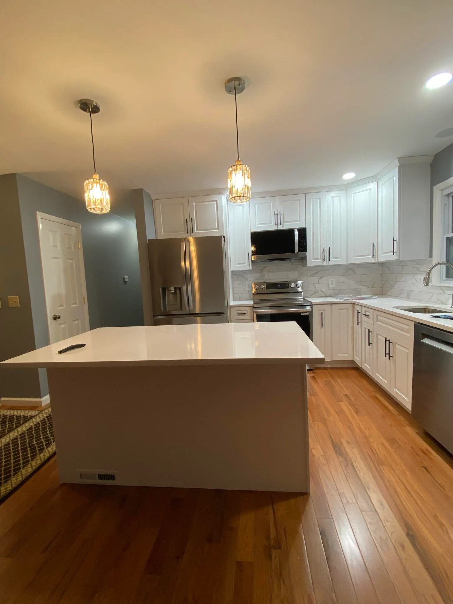 White kitchen with island, pendant lights, and hardwood floor