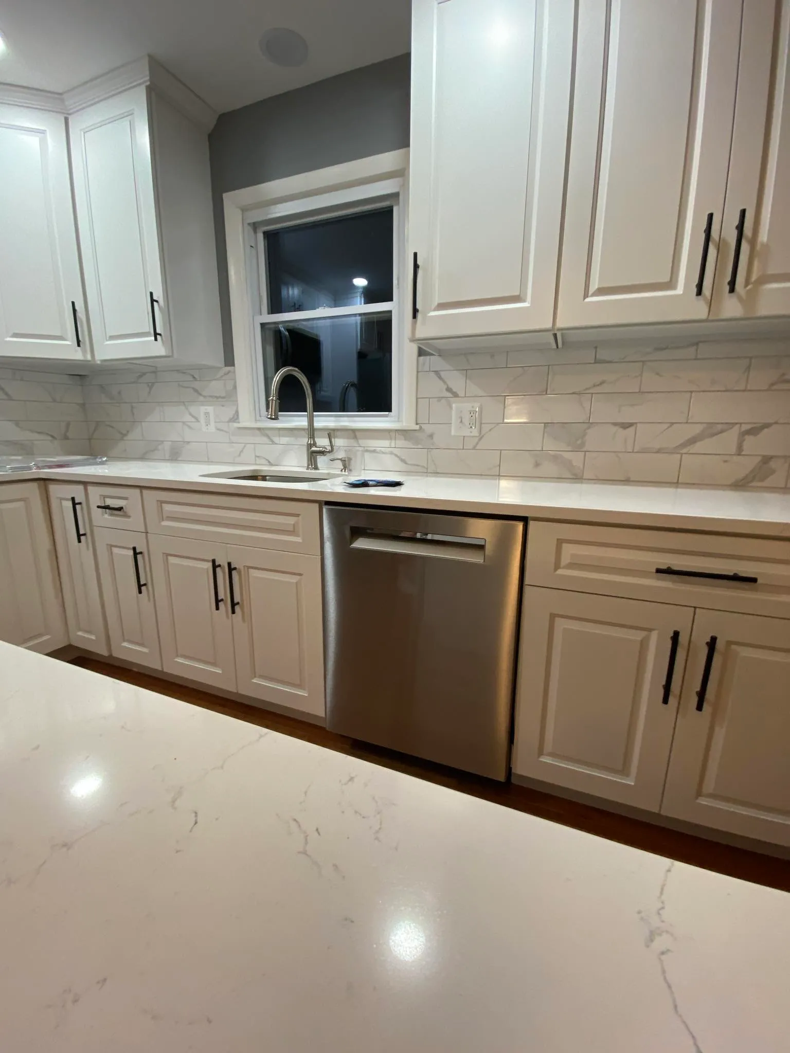 White kitchen sink area with dishwasher and marble