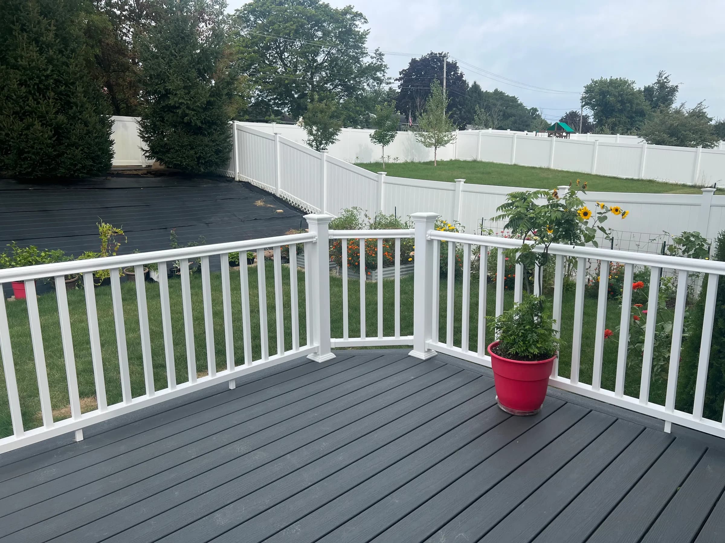 Gray composite deck corner with white railings, red potted plant, and privacy fence