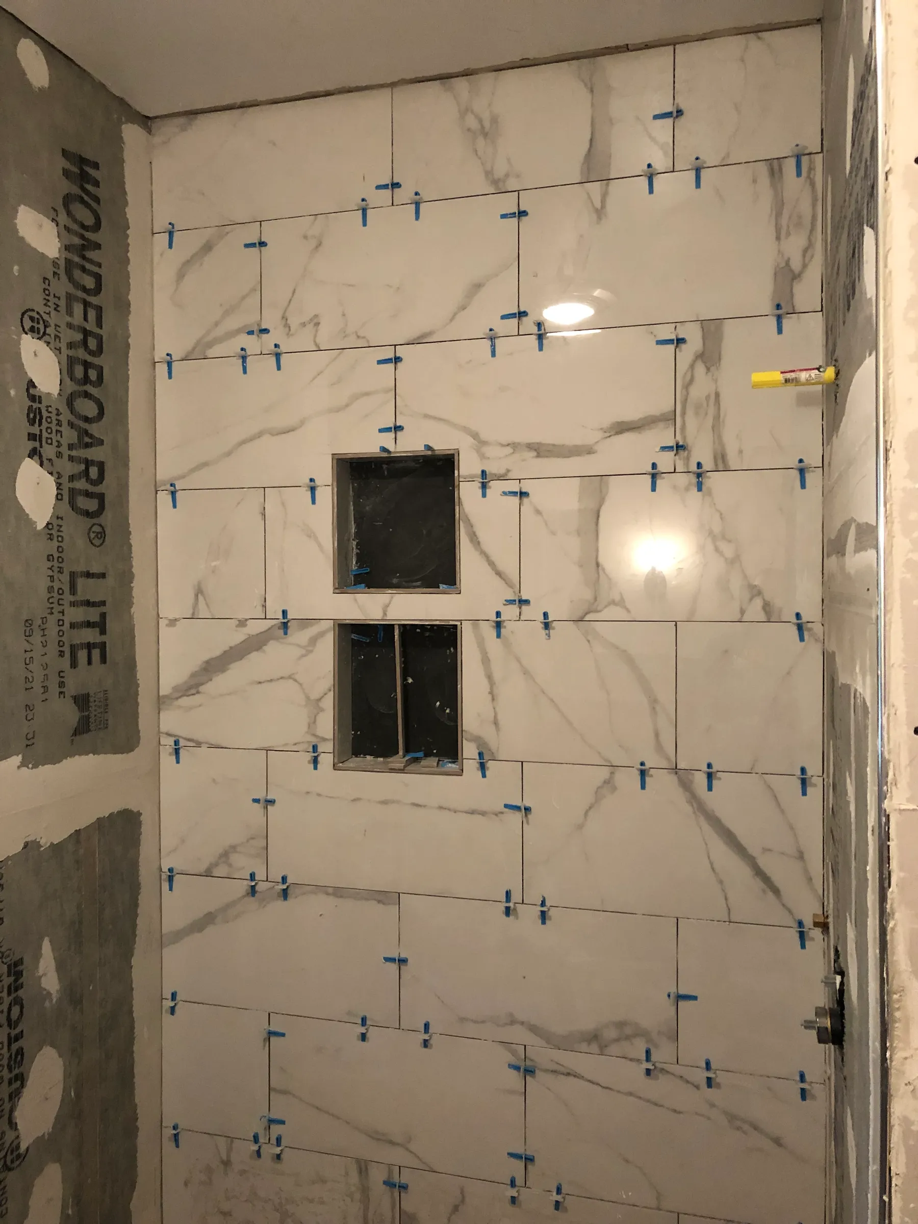 Marble tile wall installation in progress with spacers