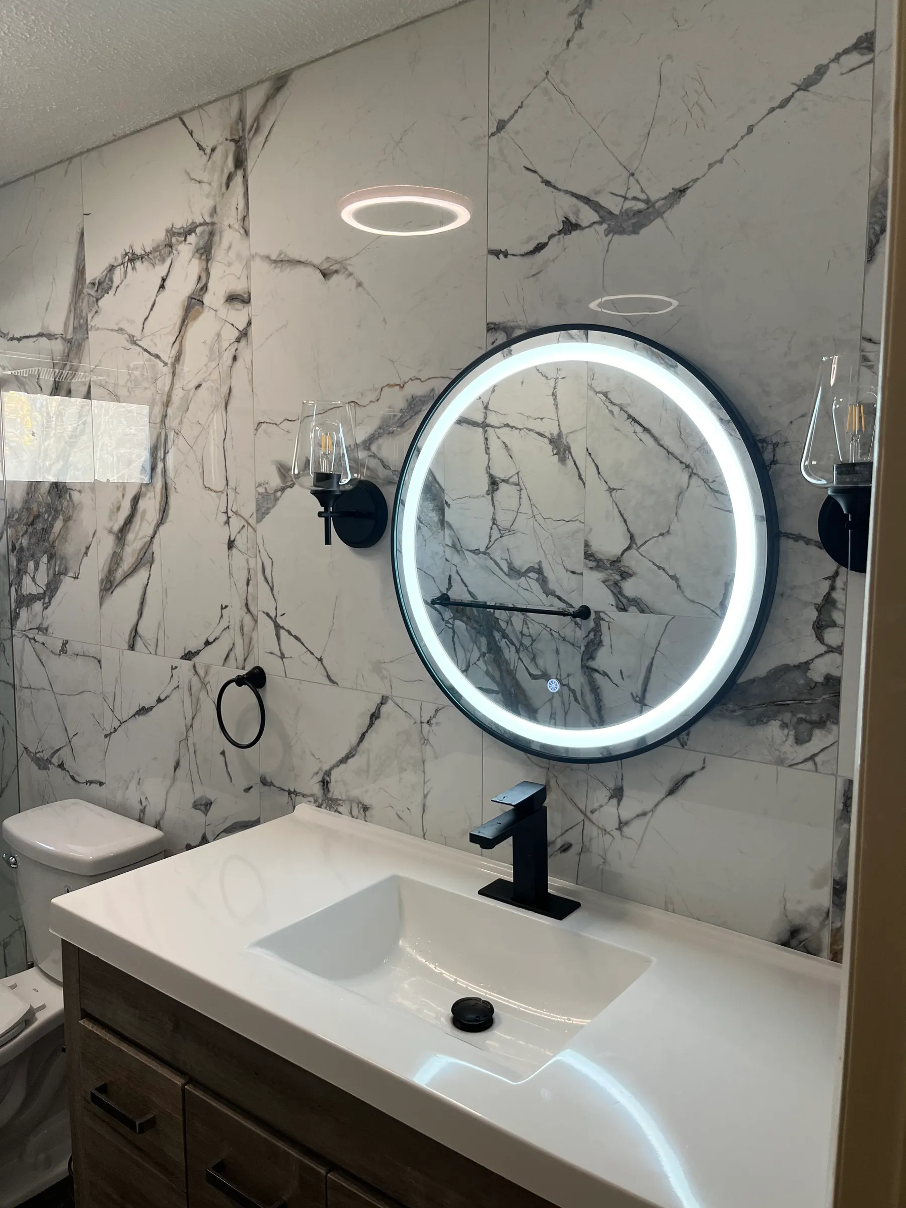 Round LED-lit mirror above floating vanity with marble wall